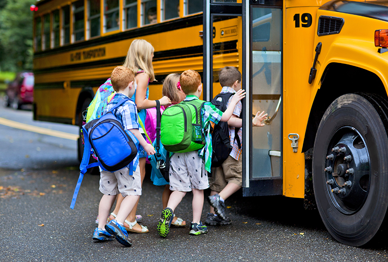 Children with backpacks getting into a school yellow bus 